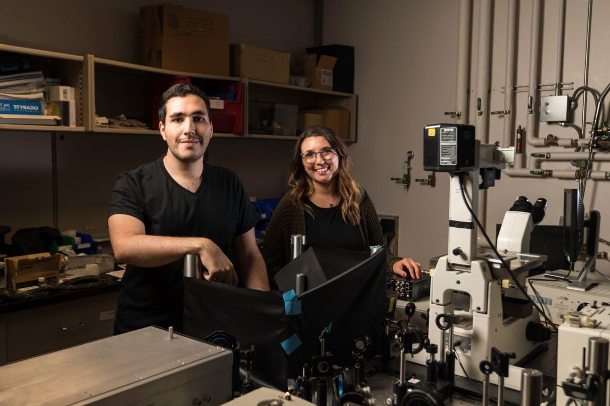 Two students in a research lab next to a giant microscope